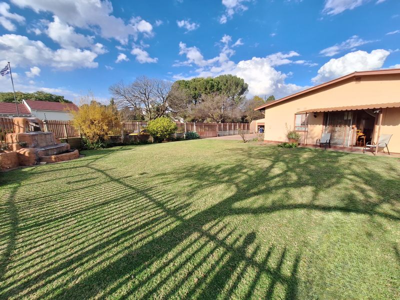 A well-maintained rear garden featuring a manicured lawn, perimeter fencing, and a decorative stone water feature adjacent to the home's patio area.