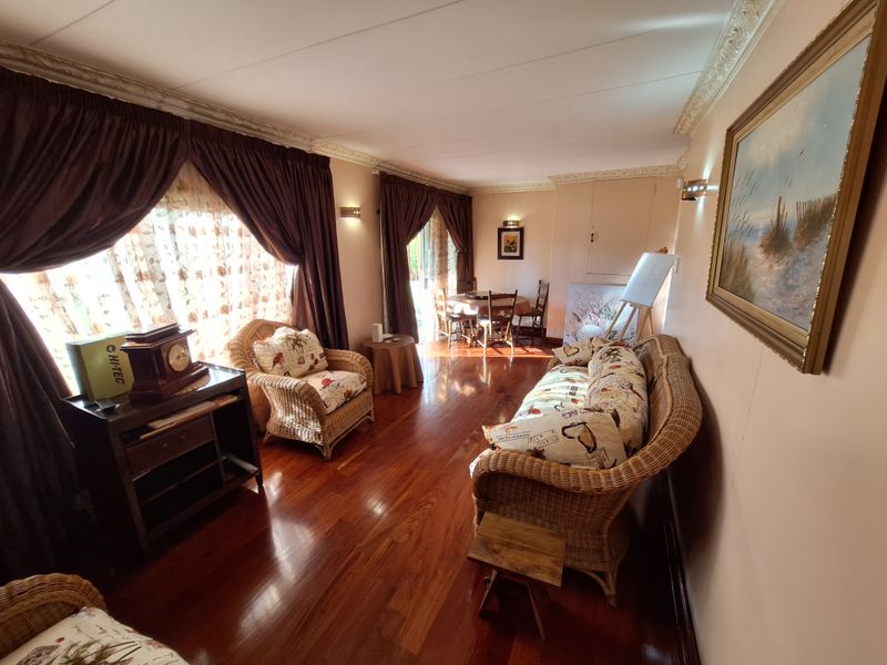 A spacious living room featuring polished hardwood flooring, decorative crown molding, and wall sconce lighting, offering a warm and inviting atmosphere.