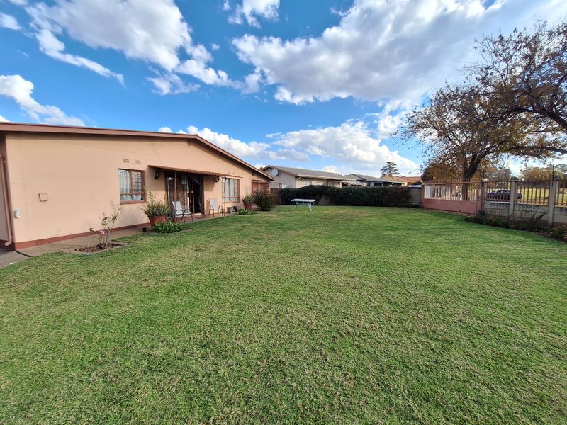 A spacious rear garden featuring a well-maintained lawn, perimeter fencing, and a rear building elevation with a sliding door and awning.