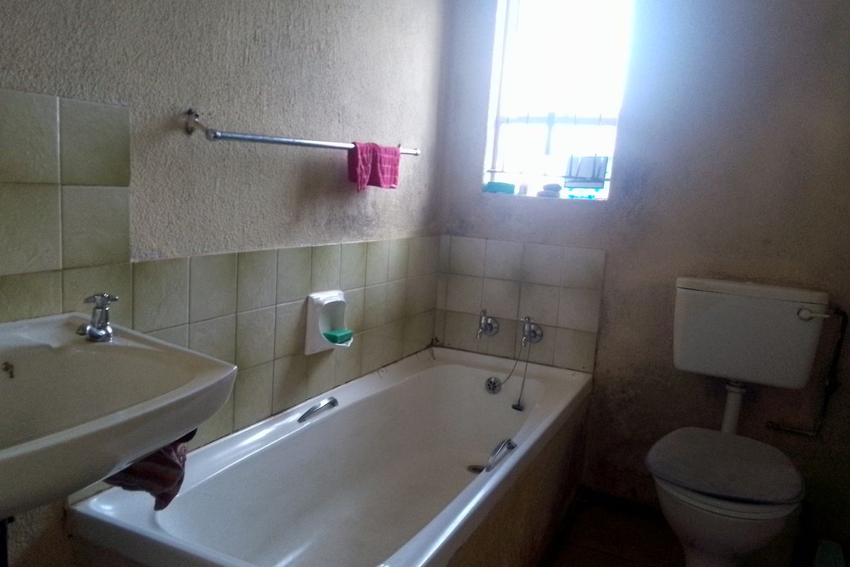 A dated bathroom featuring a standard bathtub, wall-mounted basin, and toilet, requiring cosmetic updates and maintenance to improve its overall condition.