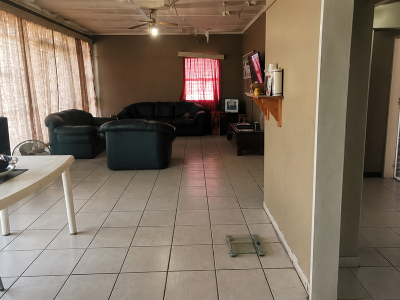 Spacious open-plan living area featuring tiled flooring, a ceiling fan, and direct access to adjacent rooms, requiring cosmetic updates to the ceiling and walls.