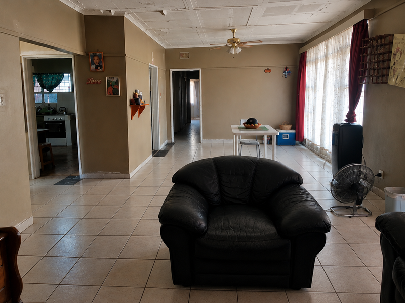 Spacious living area featuring tiled flooring, a ceiling fan, and large windows, providing a functional layout with direct access to the kitchen and hallway.