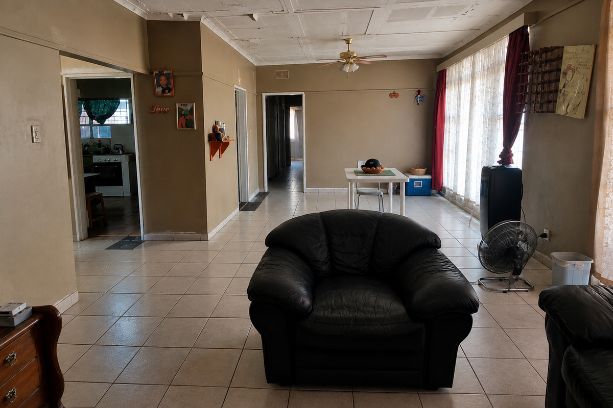 Spacious living area featuring tiled flooring, a ceiling fan, and large windows, providing a functional layout with direct access to the kitchen and hallway.