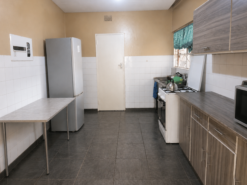 A functional kitchen featuring wood-look cabinetry, laminate countertops, a freestanding stove, and tiled flooring with a practical layout.