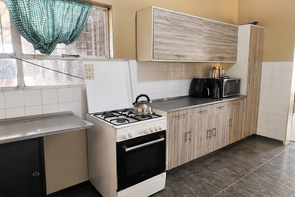 A functional kitchen featuring wood-look cabinetry, a tiled splashback, stainless steel sink, and a freestanding stove with tiled flooring throughout.