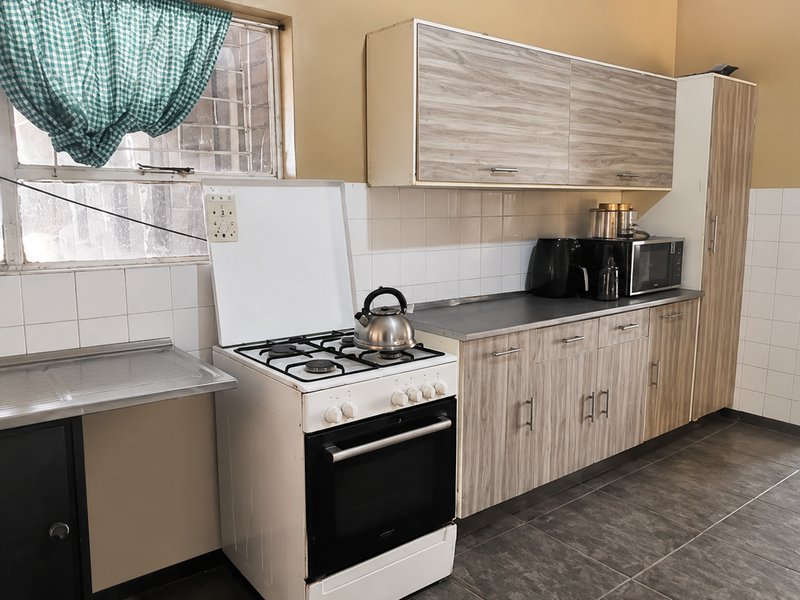 A functional kitchen featuring wood-look cabinetry, a tiled splashback, stainless steel sink, and a freestanding stove with tiled flooring throughout.