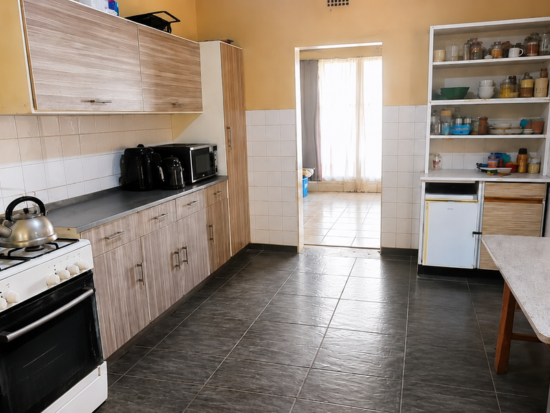 A functional kitchen featuring wood-look cabinetry, a gas stove, tiled backsplash, and dark floor tiles, offering a practical layout with an adjacent transition area.