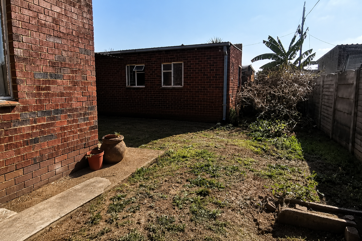 Rear exterior view of the property featuring brick walls, a concrete pathway, and a private garden area enclosed by a precast concrete boundary wall.