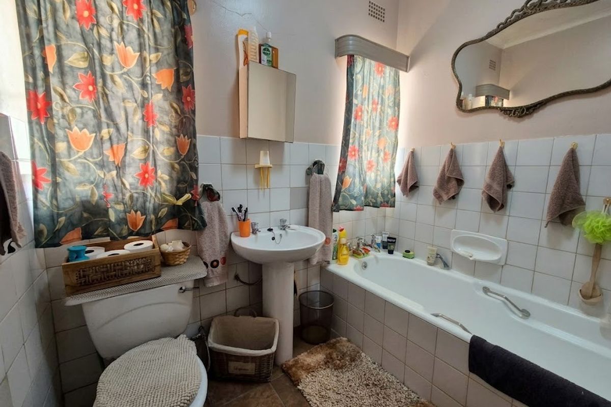 A dated bathroom featuring a pedestal basin, built-in bathtub, and ceramic tiling, currently showing signs of wear and requiring cosmetic updates.