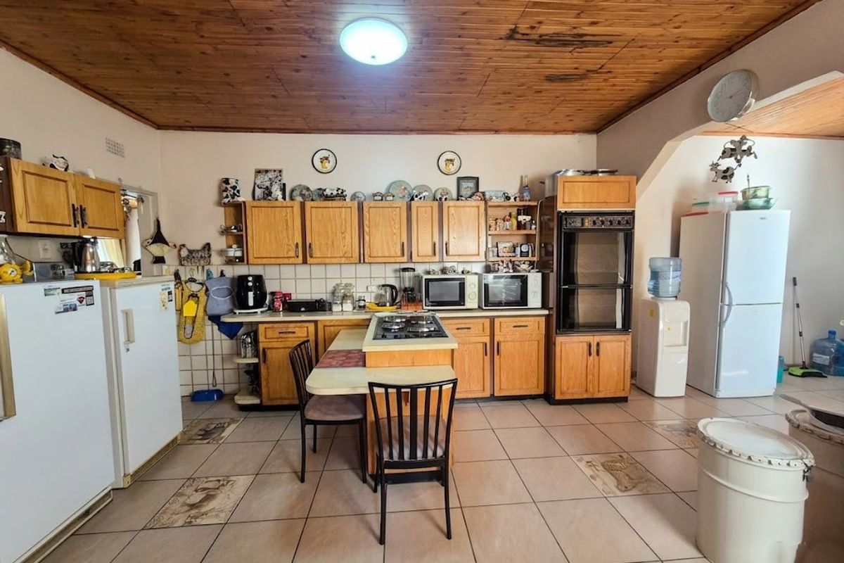 Spacious kitchen featuring wooden cabinetry, a central island with a gas hob, built-in oven, and tiled flooring throughout.