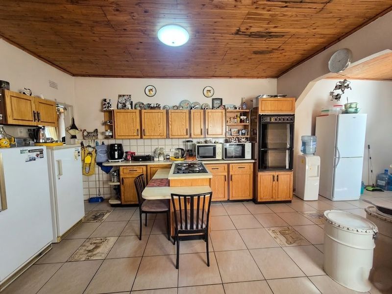 Spacious kitchen featuring wooden cabinetry, a central island with a gas hob, built-in oven, and tiled flooring throughout.