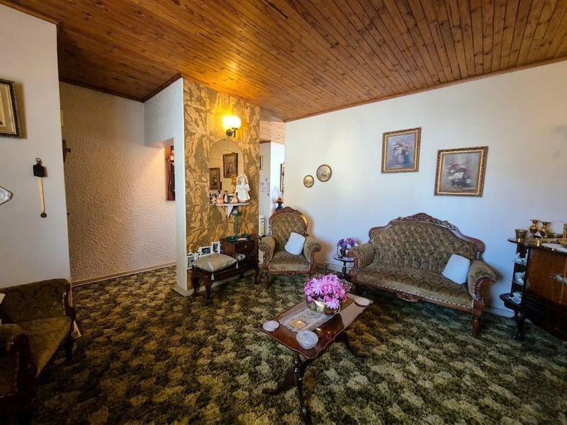 A living room featuring a timber tongue and groove ceiling, textured walls, and patterned carpeting, offering a dated aesthetic ready for modernization.