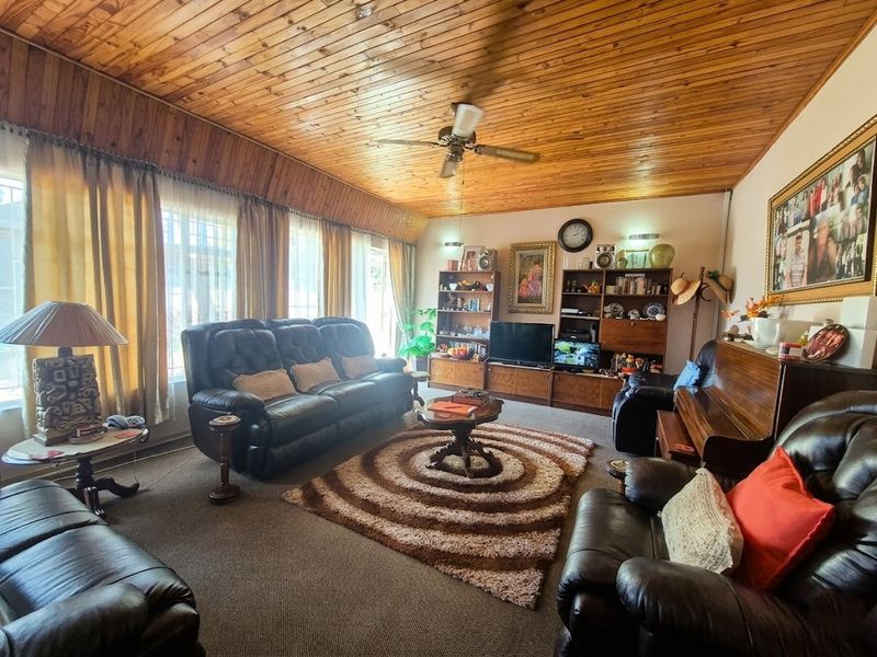 A spacious living room featuring a distinctive timber-clad ceiling, ceiling fan, and integrated built-in shelving unit, offering a warm and traditional aesthetic.