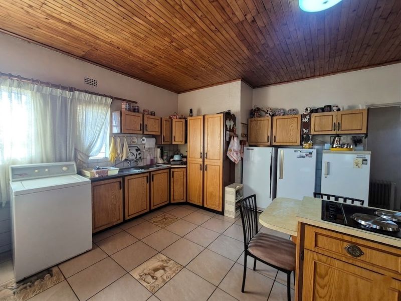 A functional kitchen featuring wooden cabinetry, tiled flooring, and a distinctive wooden ceiling, offering a traditional layout with ample storage and workspace.