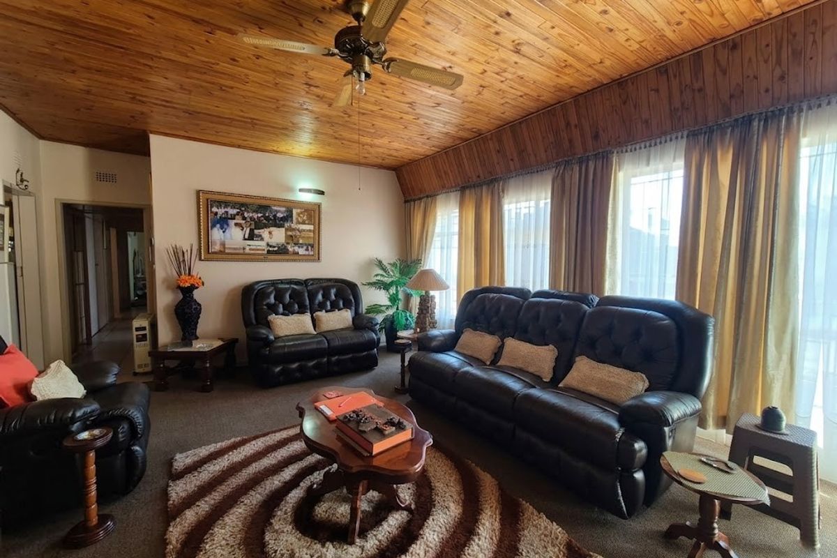 A spacious living room featuring a distinctive timber-clad ceiling, a central ceiling fan, and large windows that provide ample natural light.