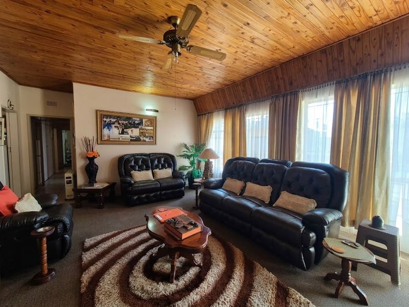 A spacious living room featuring a distinctive timber-clad ceiling, a central ceiling fan, and large windows that provide ample natural light.