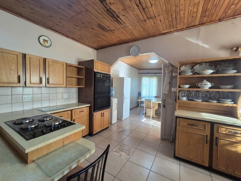 Open-plan kitchen and dining area featuring dated wooden cabinetry, a built-in oven, hob, tiled flooring, and a characteristic wooden ceiling.