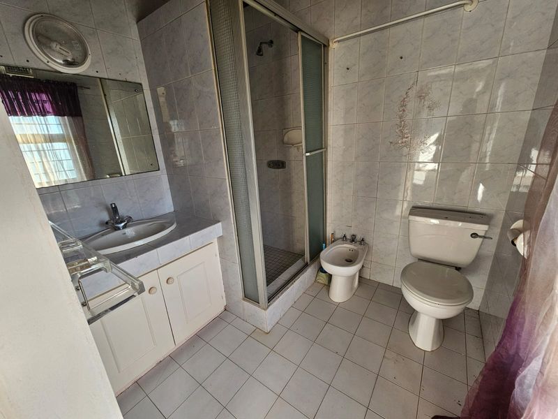 A dated bathroom featuring a shower enclosure, bidet, toilet, and vanity basin with tiled walls and flooring, requiring cosmetic updates to modernize the space.