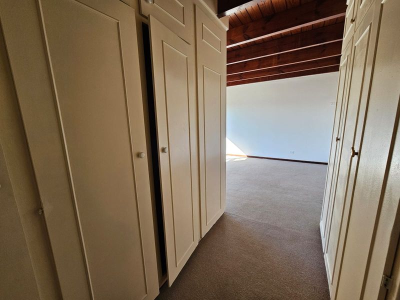 A spacious bedroom featuring built-in cupboards, carpeted flooring, and exposed timber ceiling beams, offering a clean and neutral canvas.