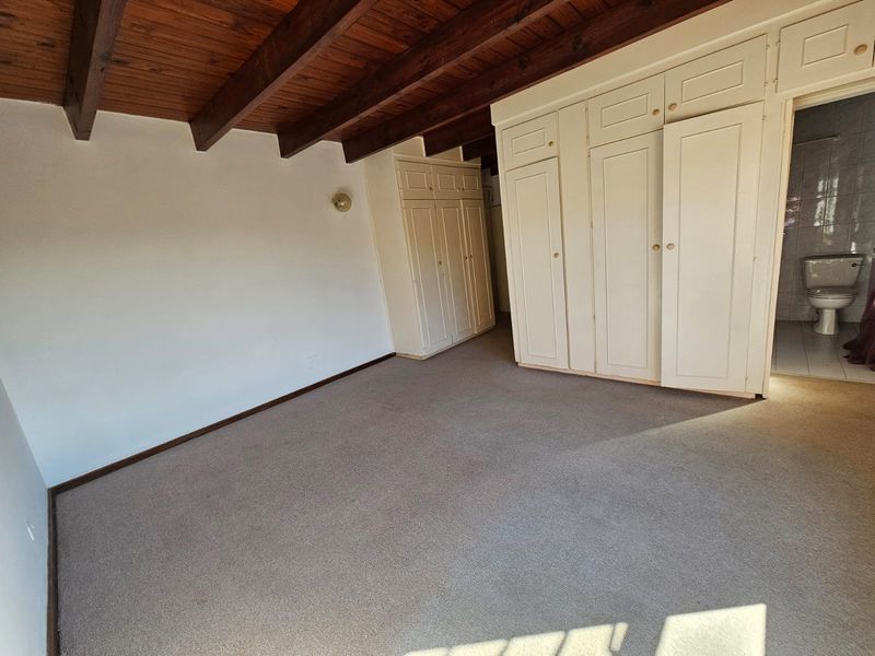 Spacious bedroom featuring exposed timber ceiling beams, extensive built-in cupboard storage, and direct access to an en-suite bathroom.