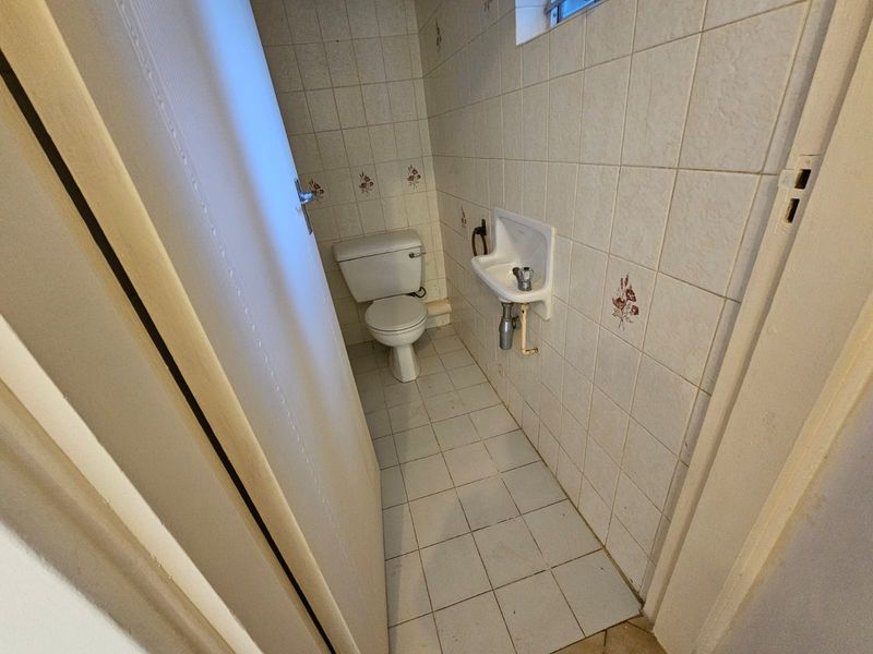 A compact guest bathroom featuring a standard toilet and wall-mounted basin with dated ceramic wall and floor tiling.