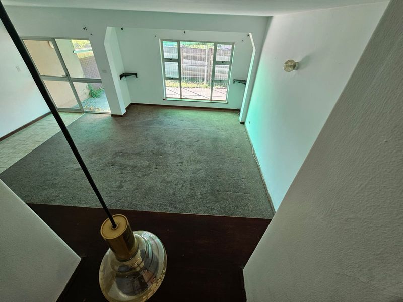 An empty living room featuring carpet flooring, large windows, and sliding glass doors leading to an outdoor area, offering a blank canvas for renovation.