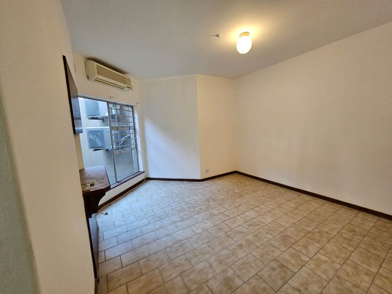 An empty bedroom featuring tiled flooring, a wall-mounted split-system air conditioner, and a window fitted with security bars.