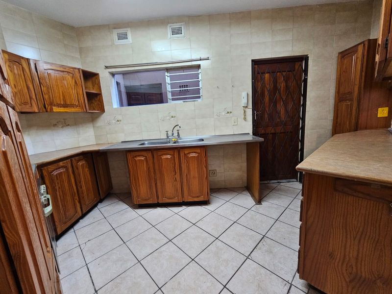 A functional kitchen featuring wooden cabinetry, tiled flooring, and a double sink, offering a practical layout ready for modern updates.