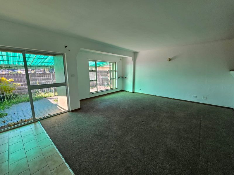 Spacious, empty living area featuring large windows, sliding glass door access to the patio, and neutral finishes ready for renovation.