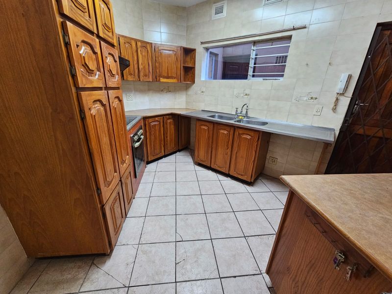 A dated kitchen featuring wooden cabinetry, tiled flooring with visible cracks, a double basin sink, and a built-in oven.