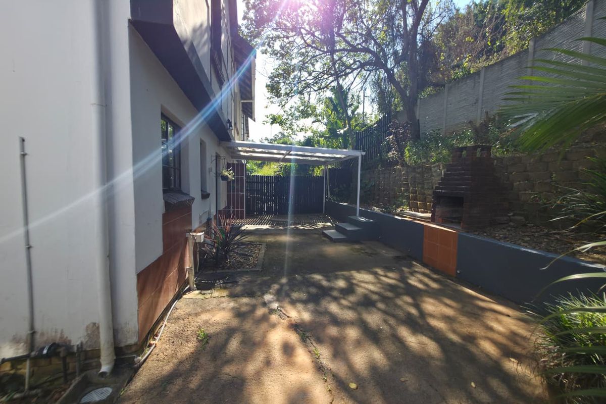 Rear exterior area featuring a built-in braai, retaining wall, and covered patio space with concrete paving.