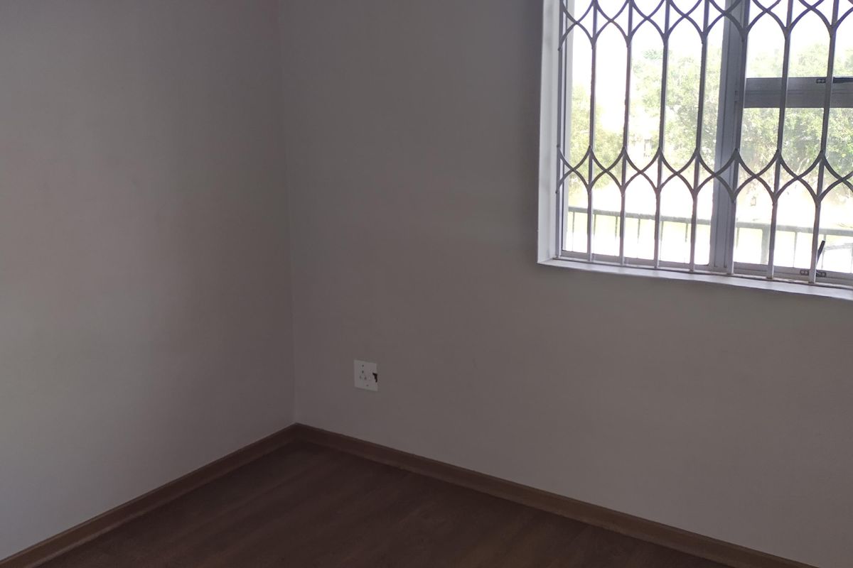 A clean, empty bedroom featuring wood-look laminate flooring and a window fitted with a security gate.