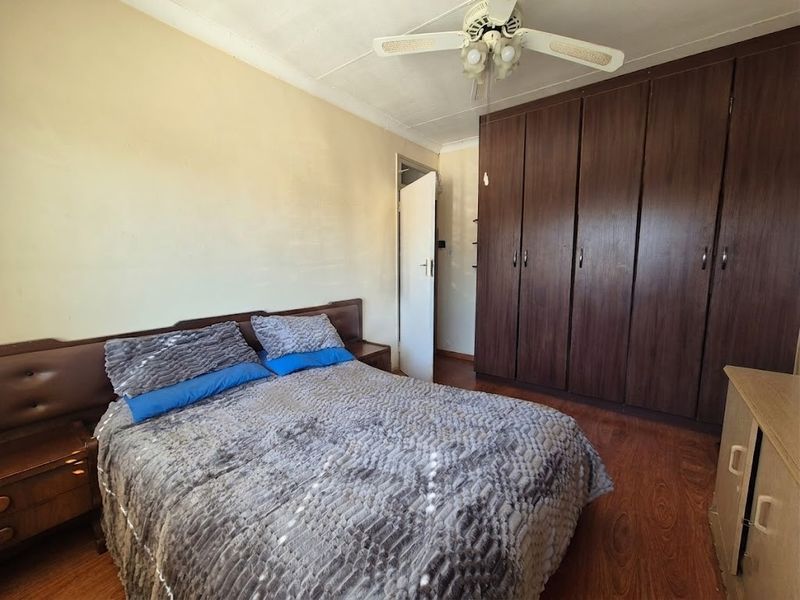 A bedroom featuring dark wood built-in cupboards, laminate flooring, and a ceiling fan, offering a functional space with potential for cosmetic updates.