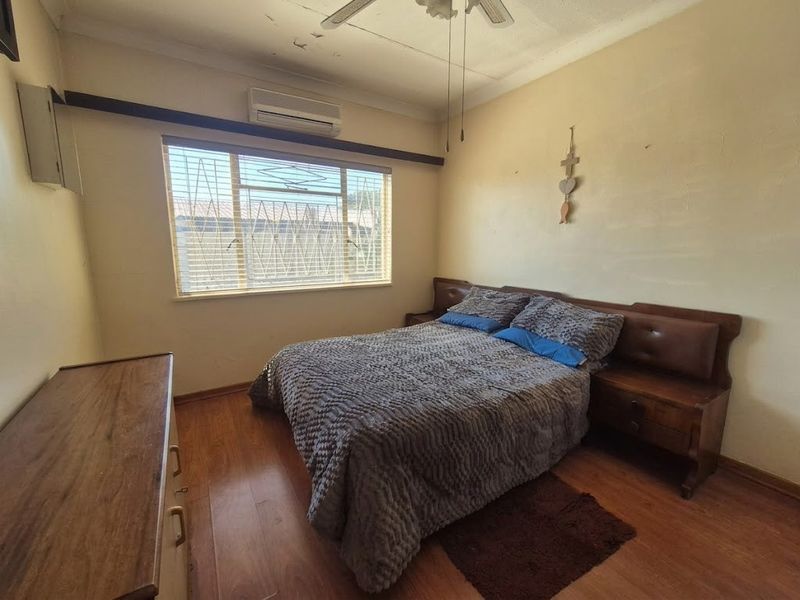 A bedroom featuring laminate flooring, a ceiling fan, and a wall-mounted air conditioning unit, requiring cosmetic updates to the walls and ceiling.