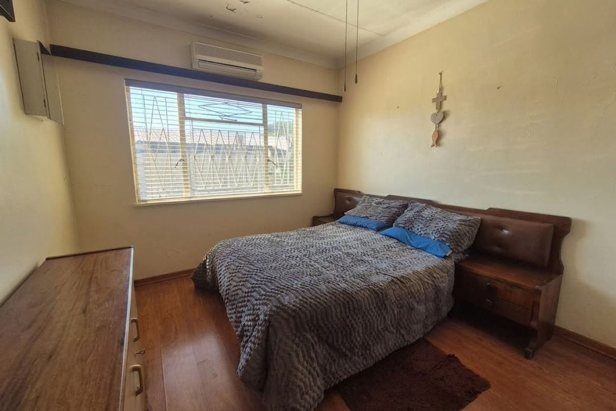 A bedroom featuring laminate flooring, a ceiling fan, and a wall-mounted air conditioning unit, requiring cosmetic updates to the walls and ceiling.