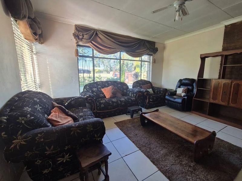 A living room featuring tiled flooring, a ceiling fan, and a brick fireplace, offering a dated interior space with potential for modernization.