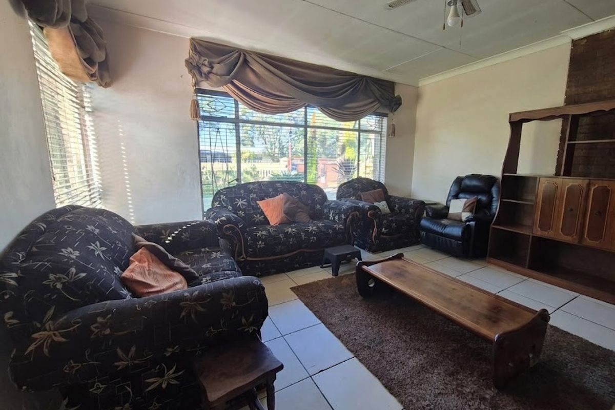 A living room featuring tiled flooring, a ceiling fan, and a brick fireplace, offering a dated interior space with potential for modernization.