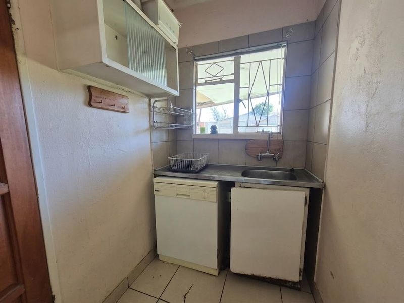 A compact scullery area featuring a stainless steel sink, tiled splashback, and built-in cabinetry, requiring cosmetic updates to improve its overall condition.