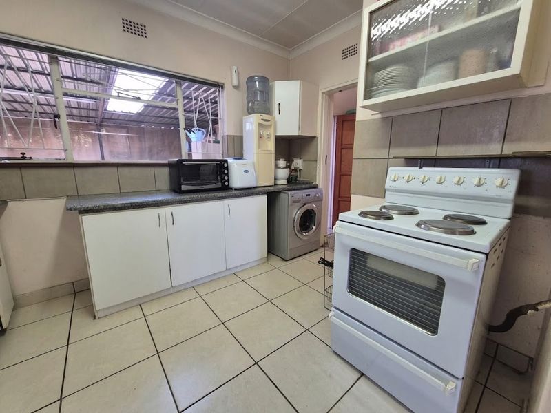 A functional kitchen featuring white cabinetry, stone countertops, tiled flooring, and a freestanding electric stove with a tiled backsplash.