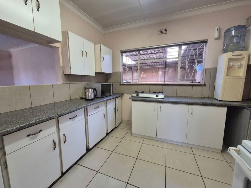 Functional kitchen featuring granite countertops, white cabinetry, tiled flooring, and a tiled backsplash with a window overlooking the exterior.