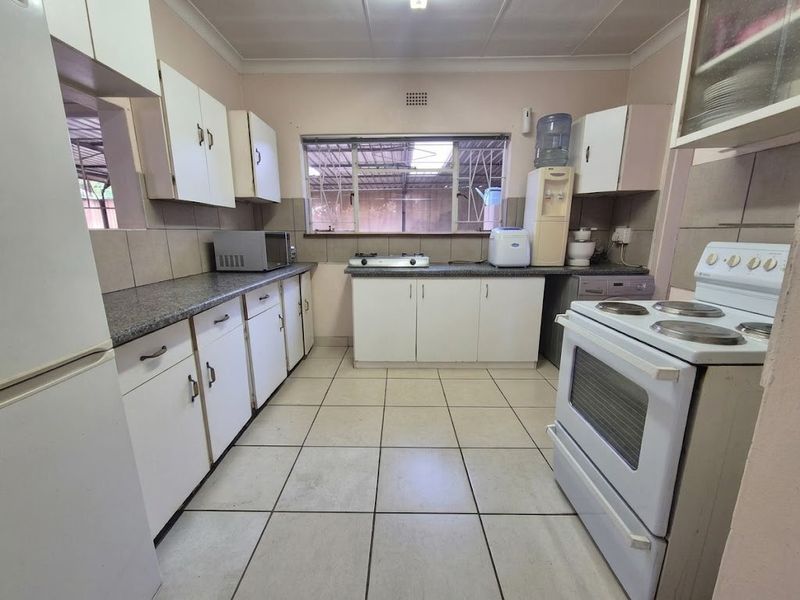 A functional kitchen featuring white built-in cabinetry, laminate countertops, tiled flooring, and a freestanding electric stove with a tiled backsplash.