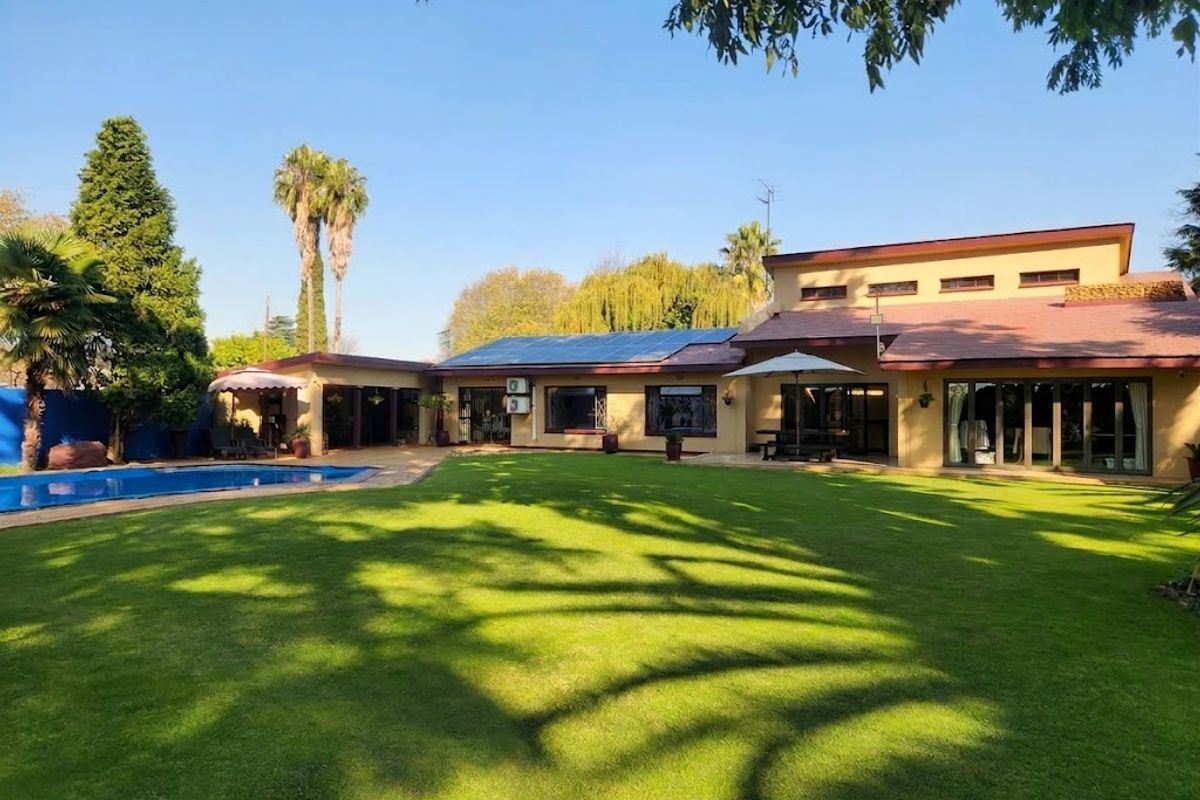 Spacious rear garden featuring a well-maintained lawn, swimming pool, and a large house exterior with solar panels and expansive sliding glass doors.
