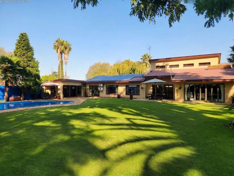 Spacious rear garden featuring a well-maintained lawn, swimming pool, and a large house exterior with solar panels and expansive sliding glass doors.