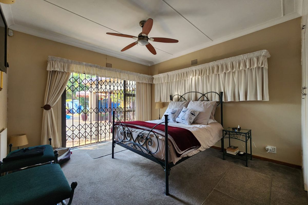 A spacious bedroom featuring a ceiling fan, carpeted flooring, and a sliding glass door with a security gate providing access to the outdoor area.