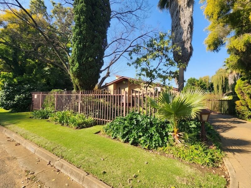 Street view of the property featuring a well-maintained garden, paved driveway, and secure metal perimeter fencing.