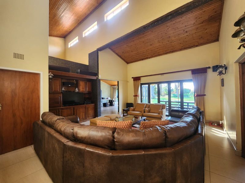 Spacious living room featuring a high vaulted timber ceiling, built-in cabinetry, brick feature wall, and large sliding doors opening to the garden.