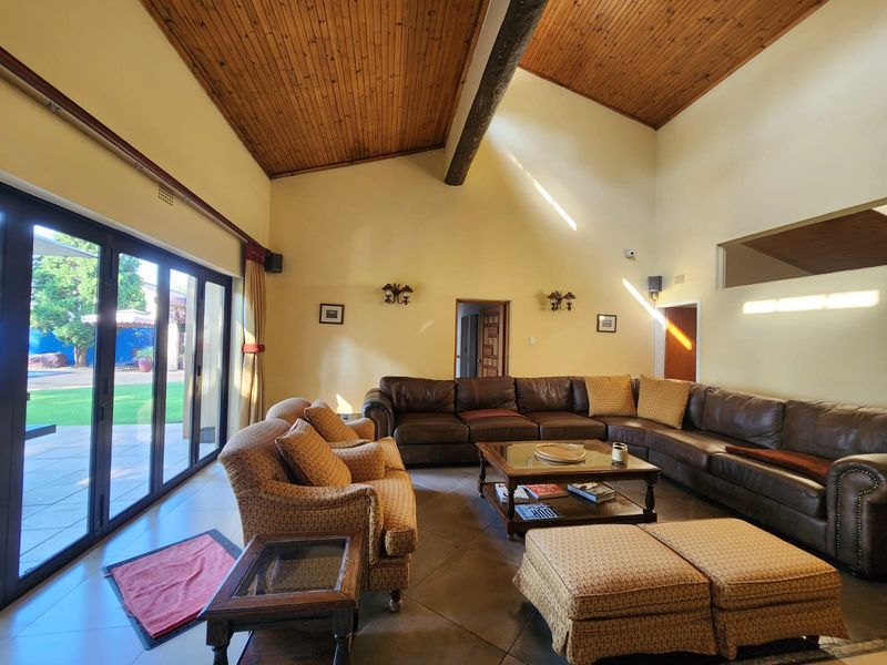 Spacious living room featuring a high vaulted timber ceiling, exposed beam, tiled floors, and large sliding glass doors providing access to the outdoor area.