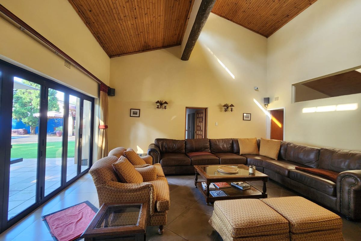 Spacious living room featuring a high vaulted timber ceiling, exposed beam, tiled floors, and large sliding glass doors providing access to the outdoor area.