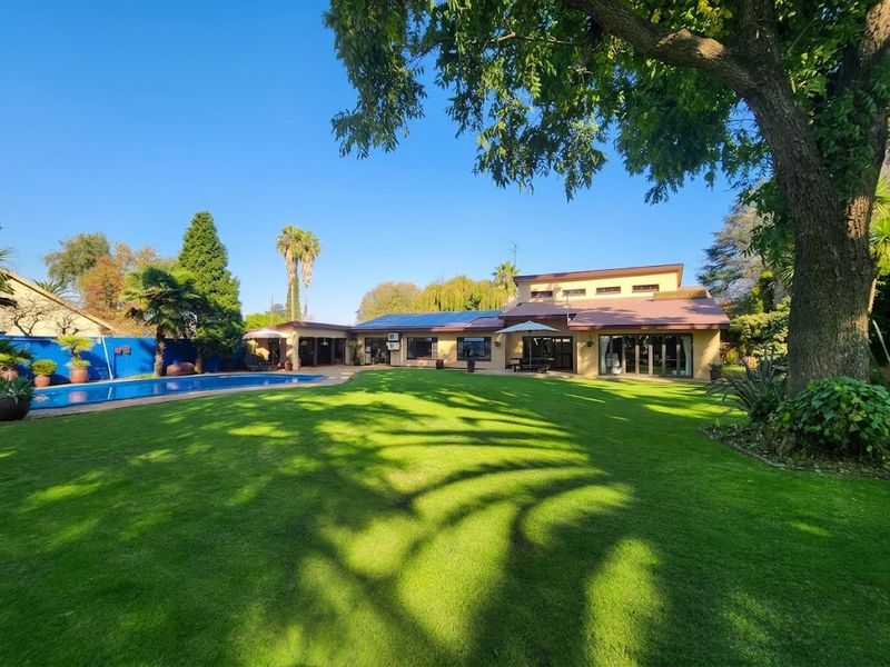 Spacious rear garden featuring a well-maintained lawn, mature trees, and a swimming pool, providing an expansive outdoor entertainment area.