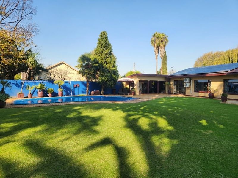 Spacious rear garden featuring a well-maintained lawn, a swimming pool with cover, and a covered patio area attached to the main house.